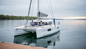 Recreational sailing catamaran at anchor near a Great Lakes shoreline with twin hulls and a spacious deck, with a family relaxing on board.